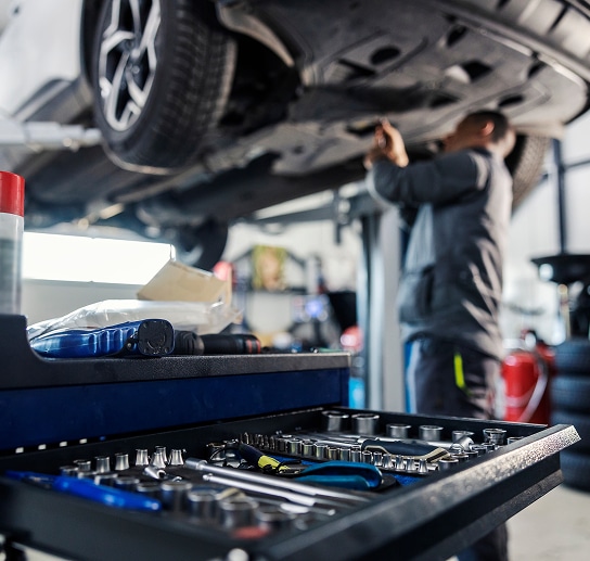 Réparation auto : mécanicien et outillage professionnel Mécanicien travaillant sous une voiture sur pont élévateur, gros plan sur un tiroir de coffre à outils rempli de clés et douilles.